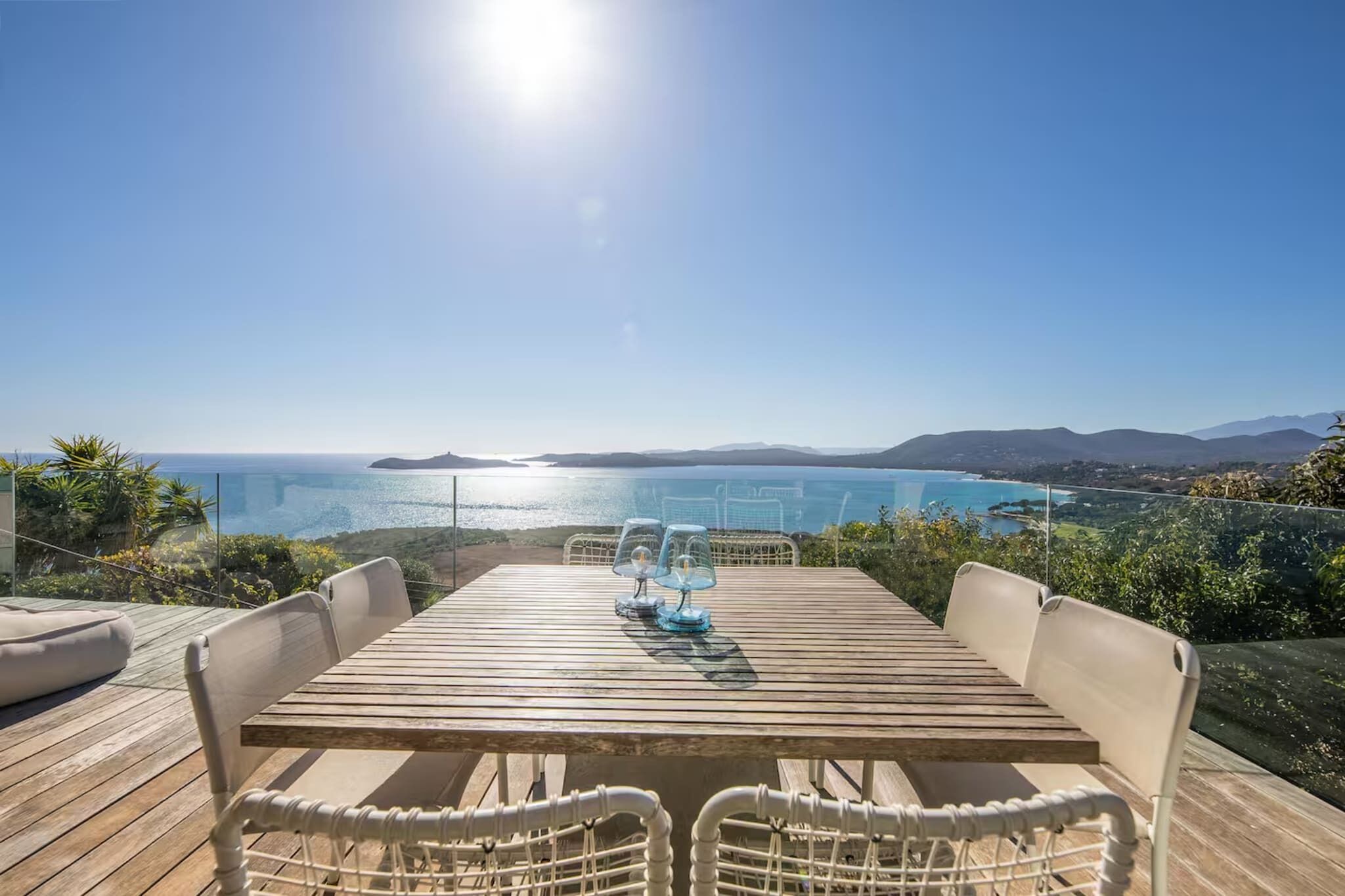 A wooden deck with a table and chairs overlooking a coastal view.