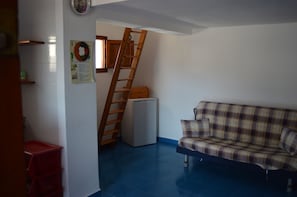A room with a blue floor, a plaid sofa, a wooden ladder, a small white refrigerator, and a red crate.