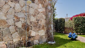 Un muro de piedra, una terraza de madera y un jardín con flores azules.