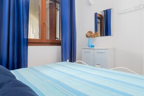 Een slaapkamer met een bed, een kaptafel, een spiegel en een raam met blauwe gordijnen.