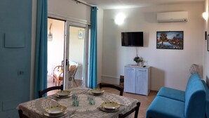 Un comedor con una mesa lista para cuatro, un sofá azul, un televisor montado en la pared y un cuadro sobre el televisor.