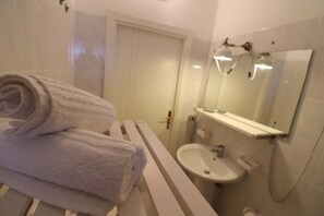 A bathroom with a white sink, a mirror, and a towel on a white bench.