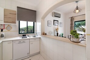 Una cocina moderna con armarios blancos, lavavajillas, ventana con vistas a zonas verdes y una lámpara colgante.
