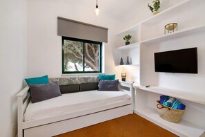 Habitación pequeña con cama, televisión, ventana con vista a árboles y repisas con adornos.