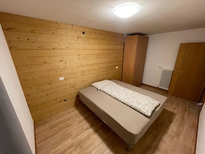 Une petite chambre avec un lit simple, des murs lambrés, un radiateur et une armoire.