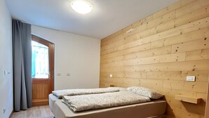 Ein Schlafzimmer mit Bett, Holzvertäfelung, einer Tür mit Vorhängen und einem Lichtschalter.