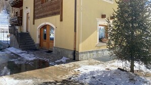 A building with a wooden facade, a small entrance, and a window with a plant. - Apartment "Piz Orsera" with Mountain View, Garden & Wi-Fi (Livigno)
