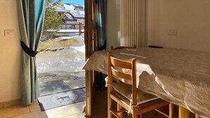 A room with a bed, a chair, a radiator, a television, and a view of a snowy landscape through a door. - Apartment "Piz Orsera" with Mountain View, Garden & Wi-Fi (Livigno)