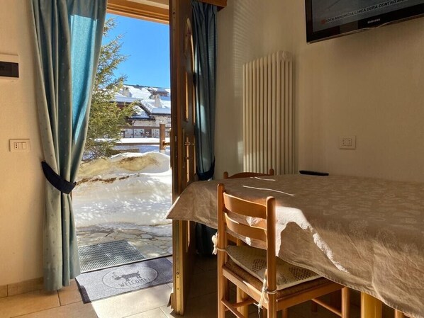 Une pièce comprenant un lit, une chaise, un radiateur, un téléviseur et une vue sur un paysage enneigé, visible à travers une porte.