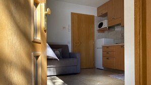 A compact living space with a kitchenette, a sofa, and a wooden door. - Apartment "Piz Orsera" with Mountain View, Garden & Wi-Fi (Livigno)