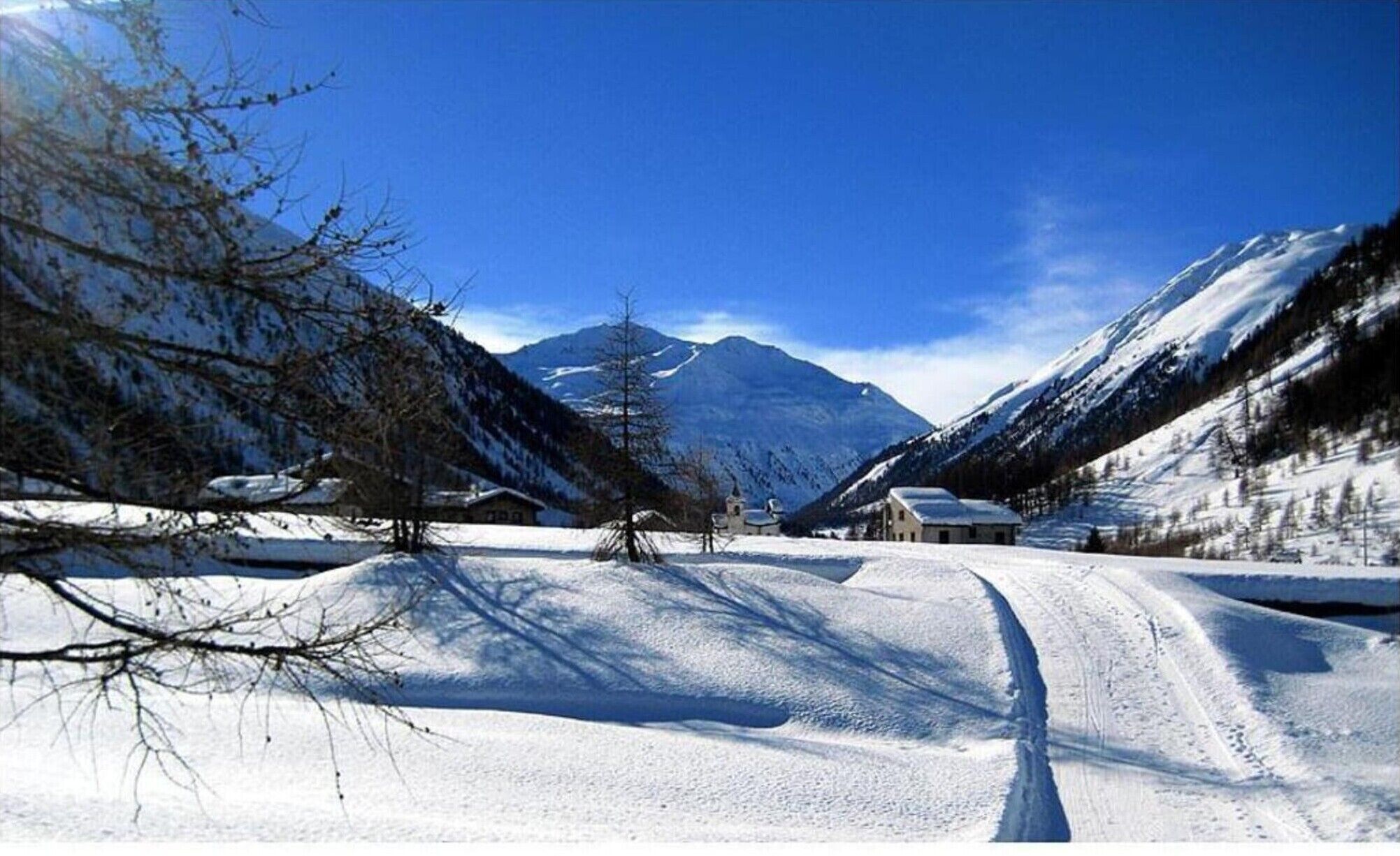 A snow-covered mountain road with buildings on either side, leading to a mountain peak.