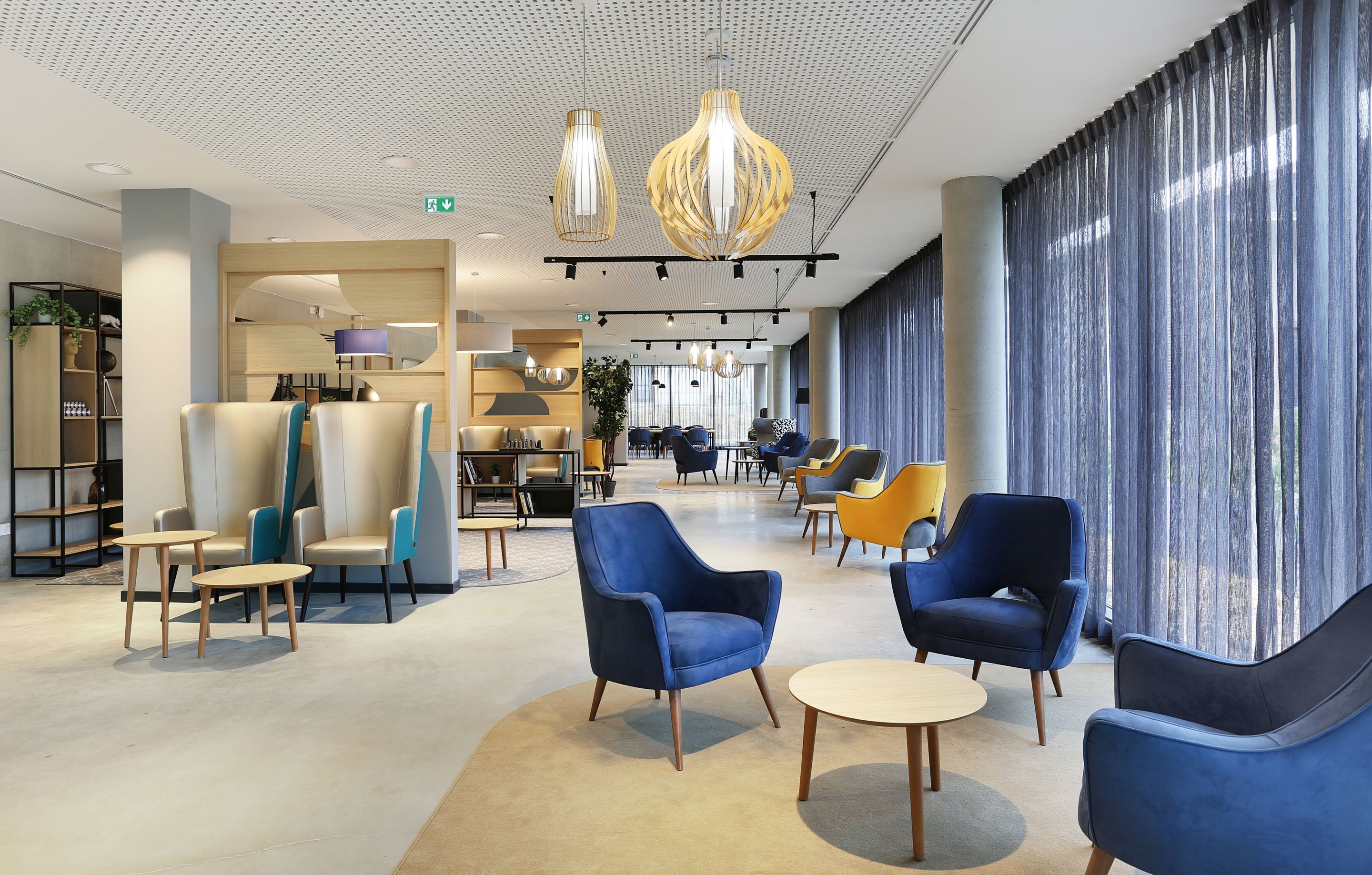 A spacious lobby with modern seating, a kitchen area, and large windows with curtains.