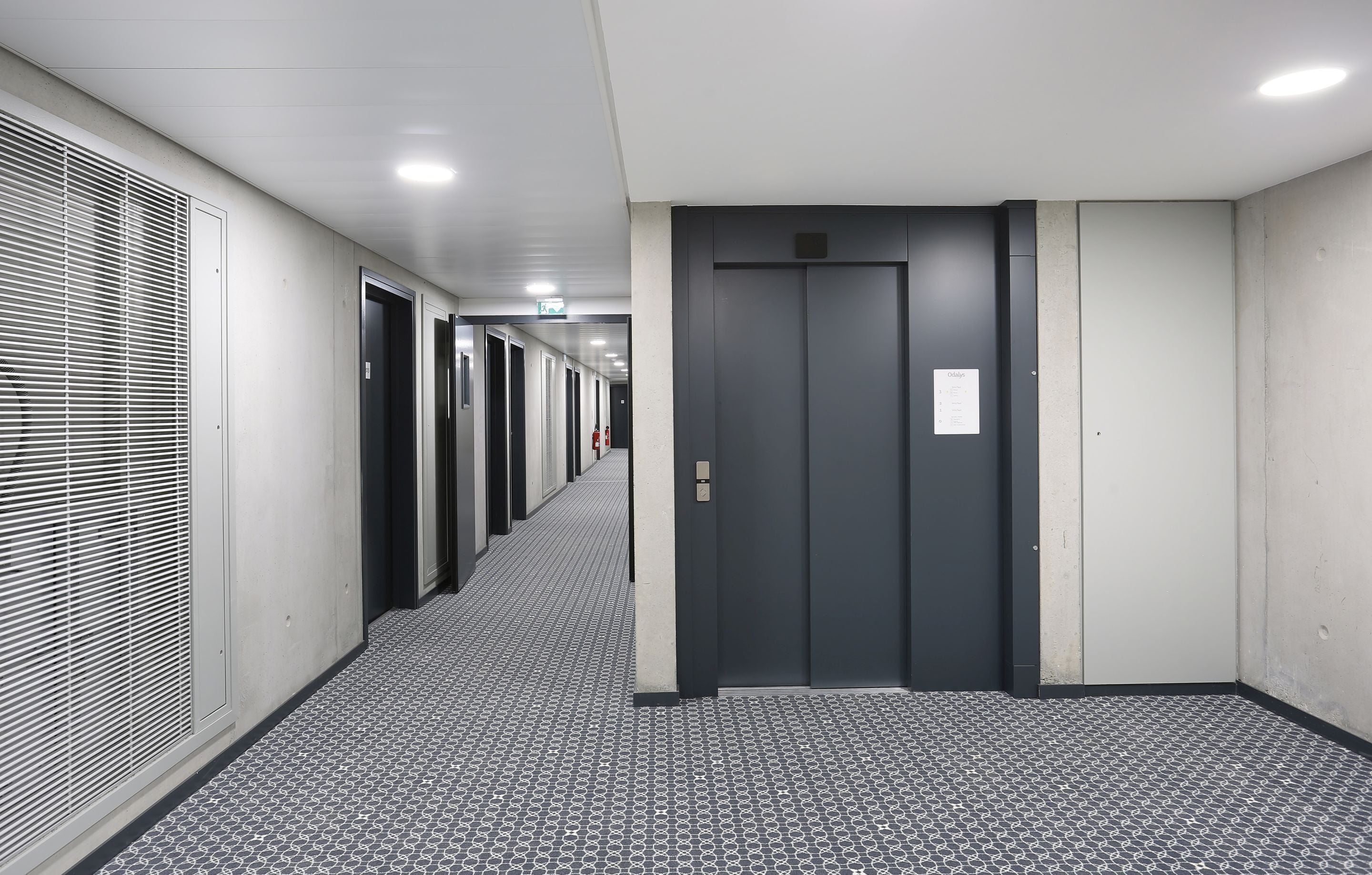 A hallway with a patterned floor, a series of doors, and an elevator.