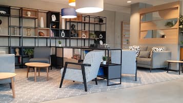 Un espace de détente moderne comprenant un canapé, des fauteuils, une petite table et une bibliothèque remplie d’objets décoratifs.