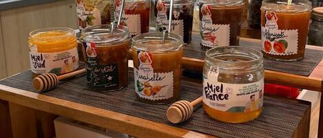 A variety of jars and bottles of honey and jam on a wooden table in a kitchen setting.