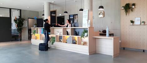 A reception area with a wooden desk, shelves with plants, and a black suitcase.