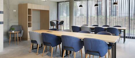 Una sala de reuniones moderna con una larga mesa, sillas azules, lámparas colgantes y amplias ventanas con persianas verticales.