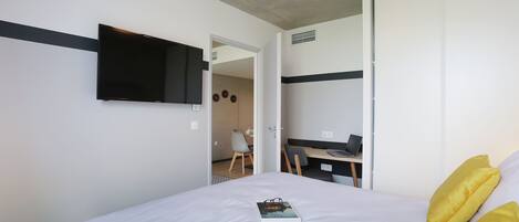 Une chambre d’hôtel moderne dotée d’un grand lit, d’un téléviseur à écran plat fixé au mur, d’un bureau avec un ordinateur portable et d’une porte donnant accès à une salle de bain.