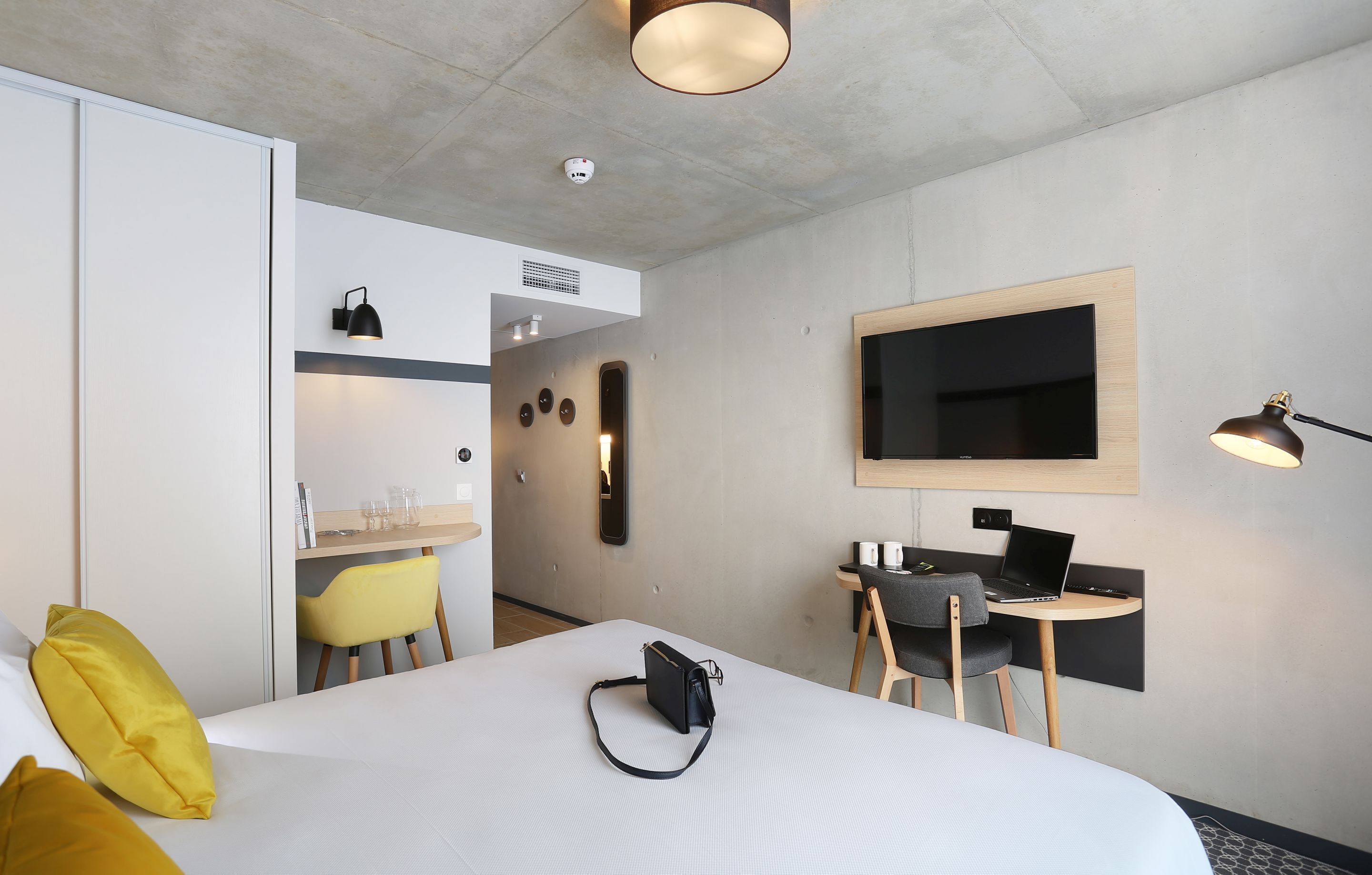 Una habitación de hotel moderna con una cama grande, un escritorio con una computadora portátil, un televisor de pantalla plana y una pequeña zona de estar.