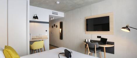 Una habitación de hotel moderna con una cama grande, un escritorio con una computadora portátil, un televisor de pantalla plana y una pequeña zona de estar.