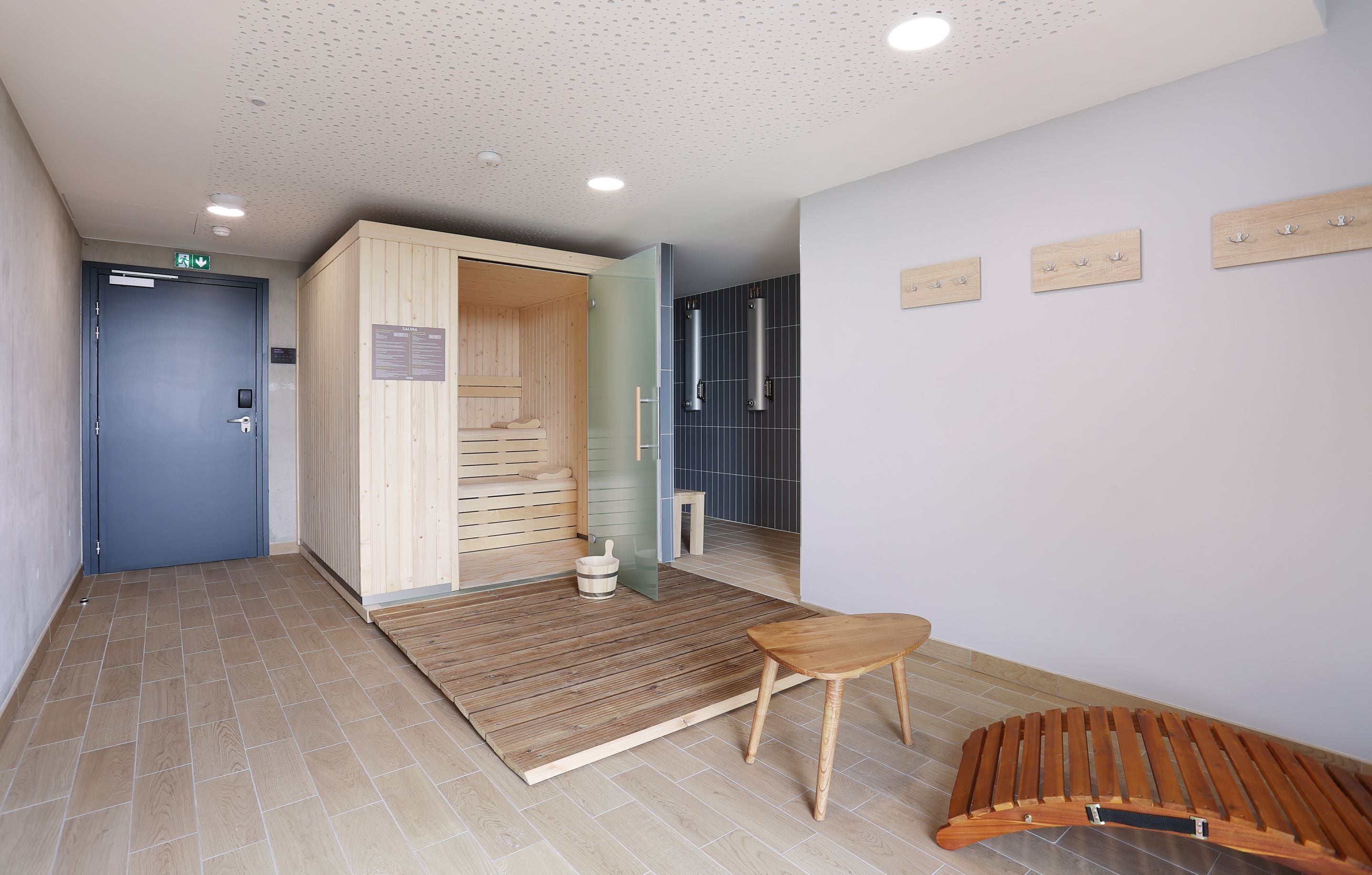 A modern interior with a wooden sauna, a small wooden bench, and a tiled floor.