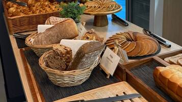 Mostrador de panadería con panes y pasteles variados, un cartel de café y un letrero que dice "Bon Appetit!".