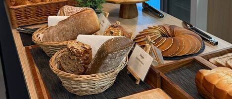 Mostrador de panadería con panes y pasteles variados, un cartel de café y un letrero que dice "Bon Appetit!".