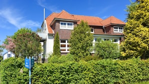 Ein zweistöckiges Haus mit rotem Ziegeldach, umgeben von üppigem Grün und blauem Himmel.