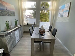 Un espace repas comprenant une longue table, des chaises, un comptoir de cuisine et des œuvres d’art accrochées aux murs.