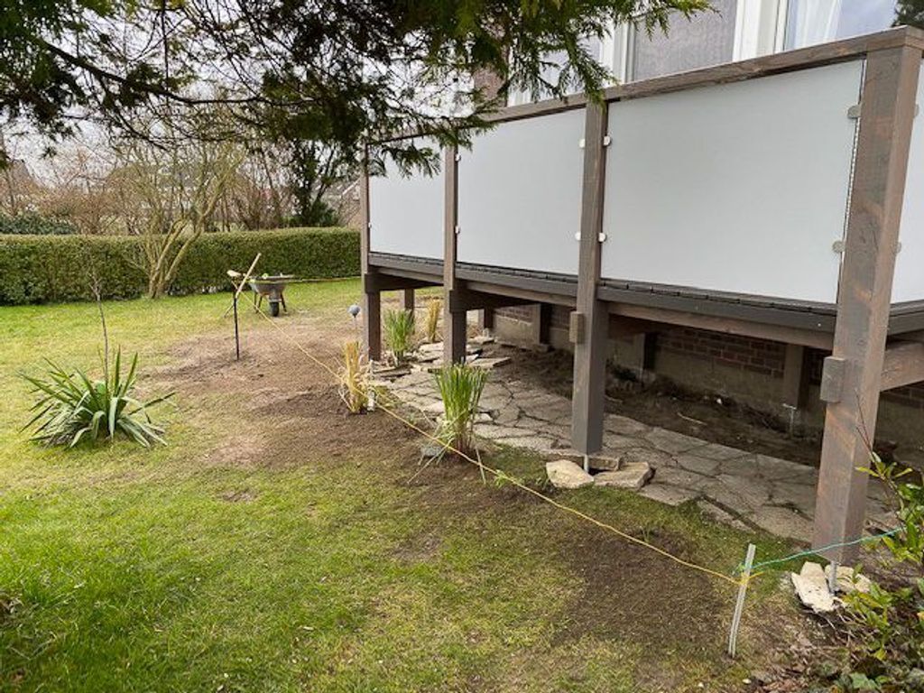 Ein Gartenbereich mit Holzdeck, Kiesweg und einer Schubkarre.