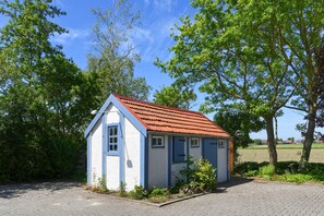 Un petit bâtiment d’un seul étage, doté d’un toit recouvert de tuiles rouges et de murs blancs, entouré de verdure et d’arbres.