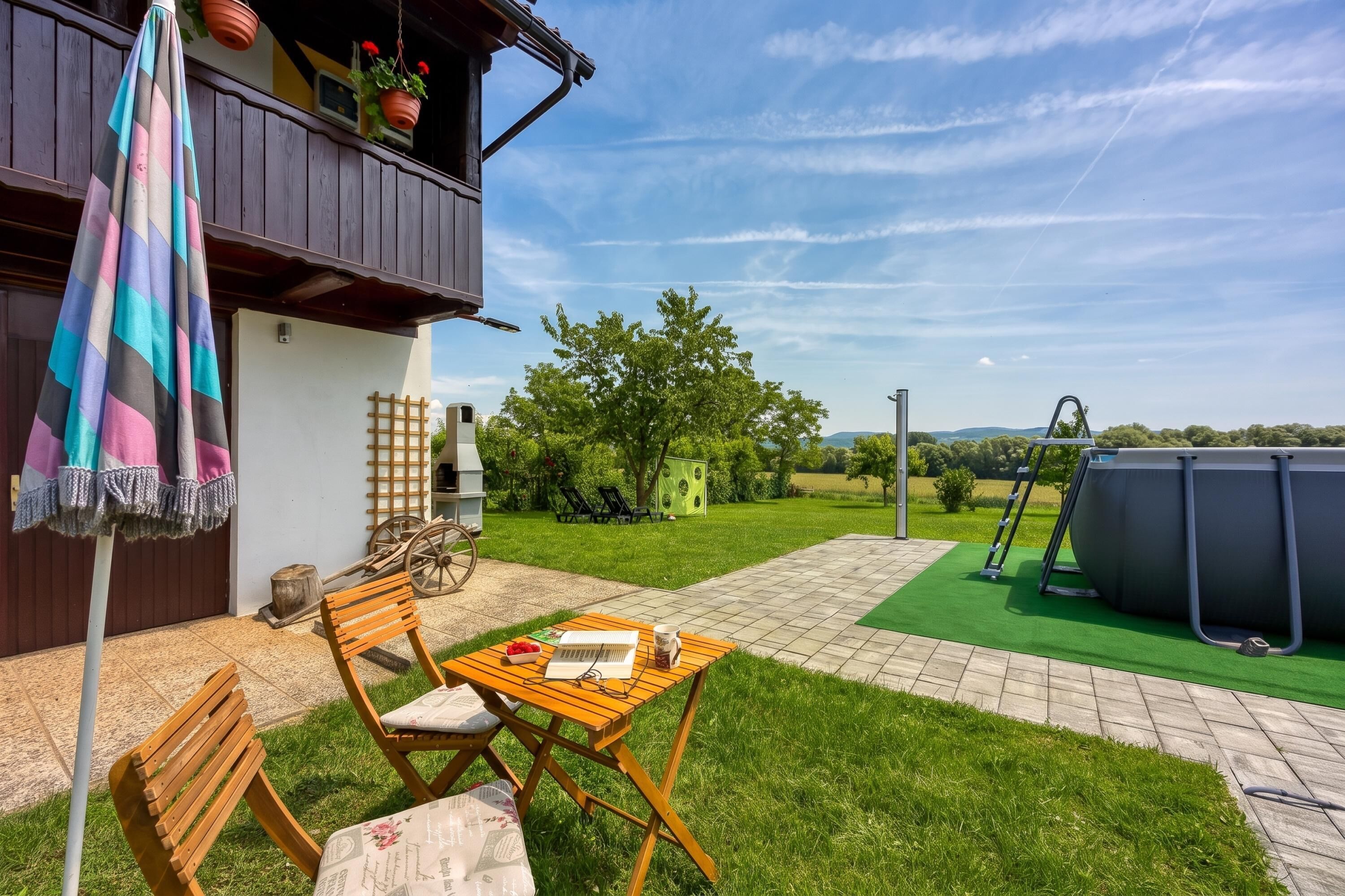 A patio with a wooden table and chairs, a hanging umbrella, and a view of a green lawn and trees.