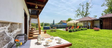A patio with a table set for tea, surrounded by a well-maintained lawn and a stone wall.