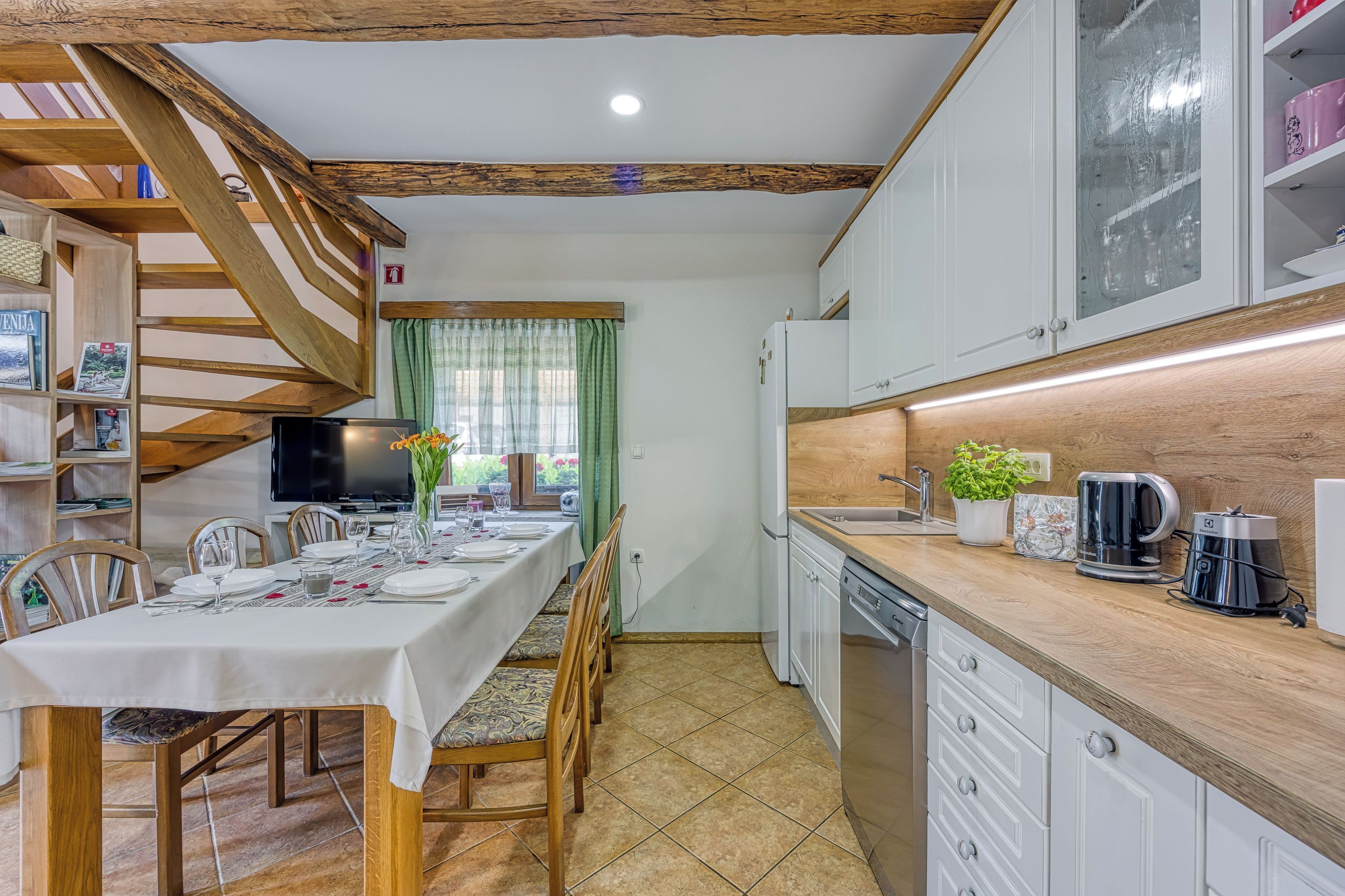 Una cocina con vigas de madera, una mesa de comedor preparada para cuatro personas y un horno empotrado.