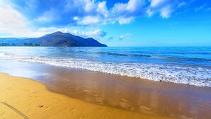 Una playa con agua azul cristalina, una orilla arenosa y una montaña al fondo.