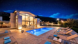 Un área moderna junto a la piscina con sillones de descanso, una pileta y un edificio con amplias ventanas.