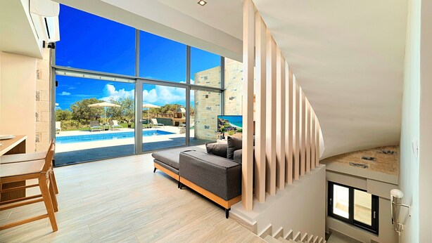 Una sala de estar moderna con un amplio ventanal que da a una zona de piscina, un sofá y una chimenea.
