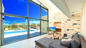 Una sala de estar moderna con un gran ventanal, un sofá gris, un televisor de pantalla plana y una chimenea de piedra.