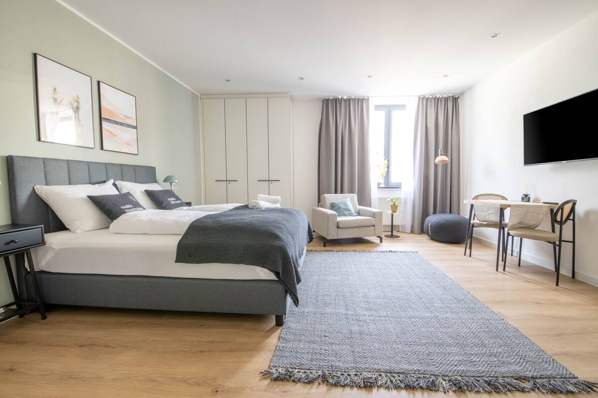A modern bedroom with a bed, bedside tables, a desk, and a TV.