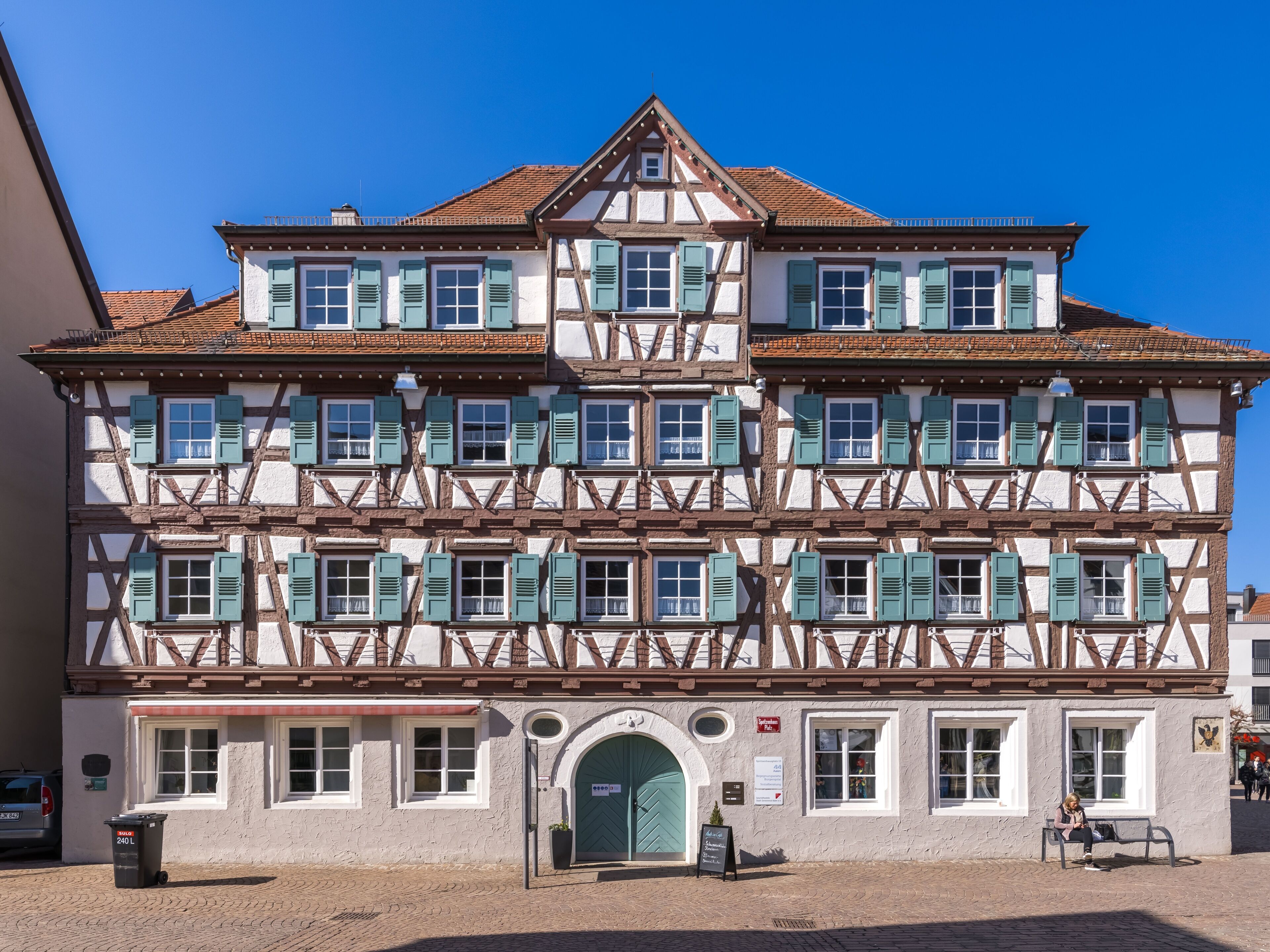A traditional half-timbered building with a green door, multiple windows with shutters, and a clear blue sky.