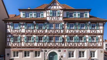 A traditional half-timbered building with a green door, multiple windows with shutters, and a clear blue sky.