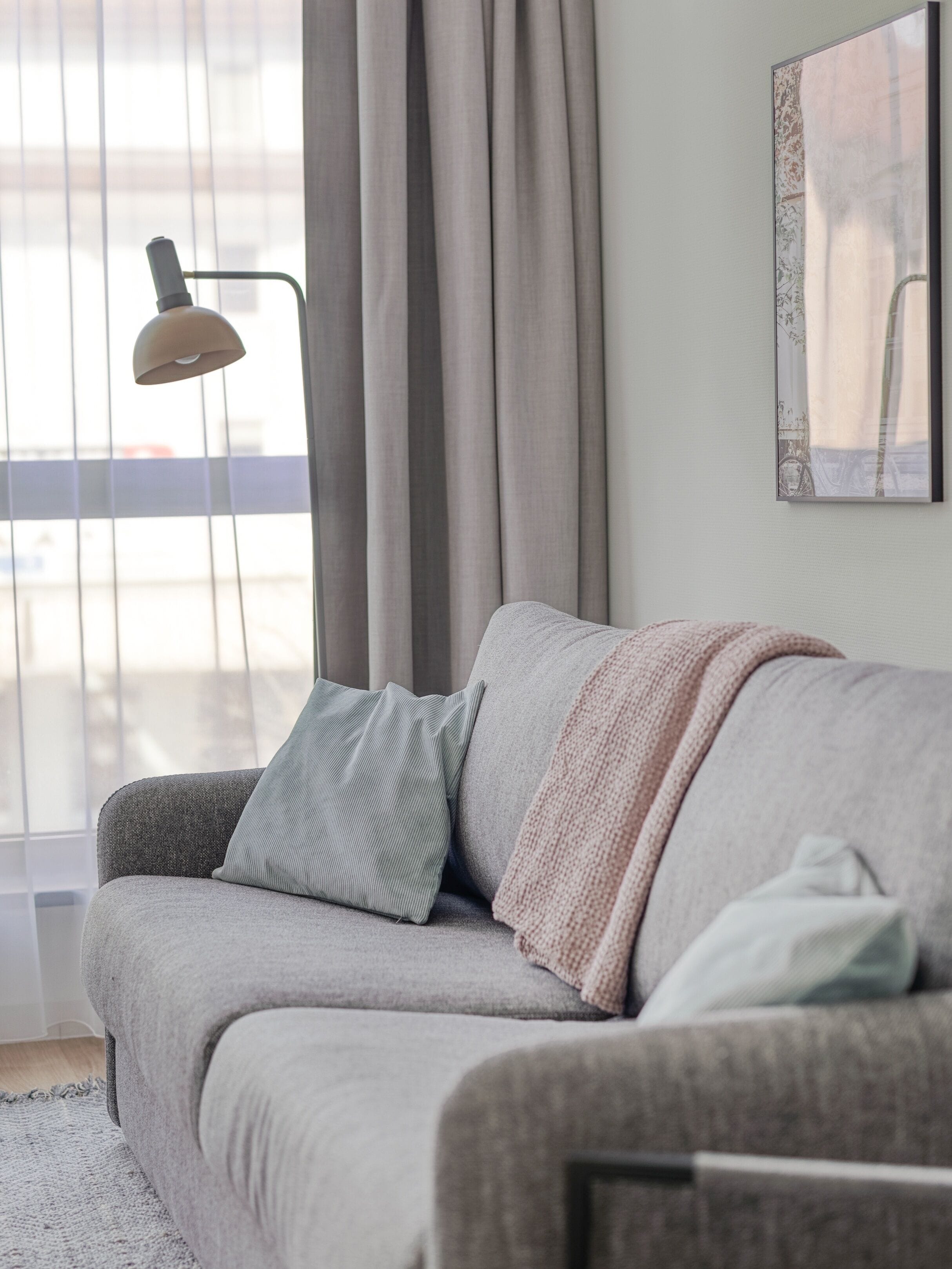 Un salon moderne avec un canapé gris, une lampe sur pied et une grande fenêtre avec des rideaux.