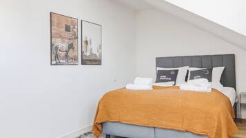 A bedroom with a bed, pillows, and a blanket. There are two framed pictures on the wall.