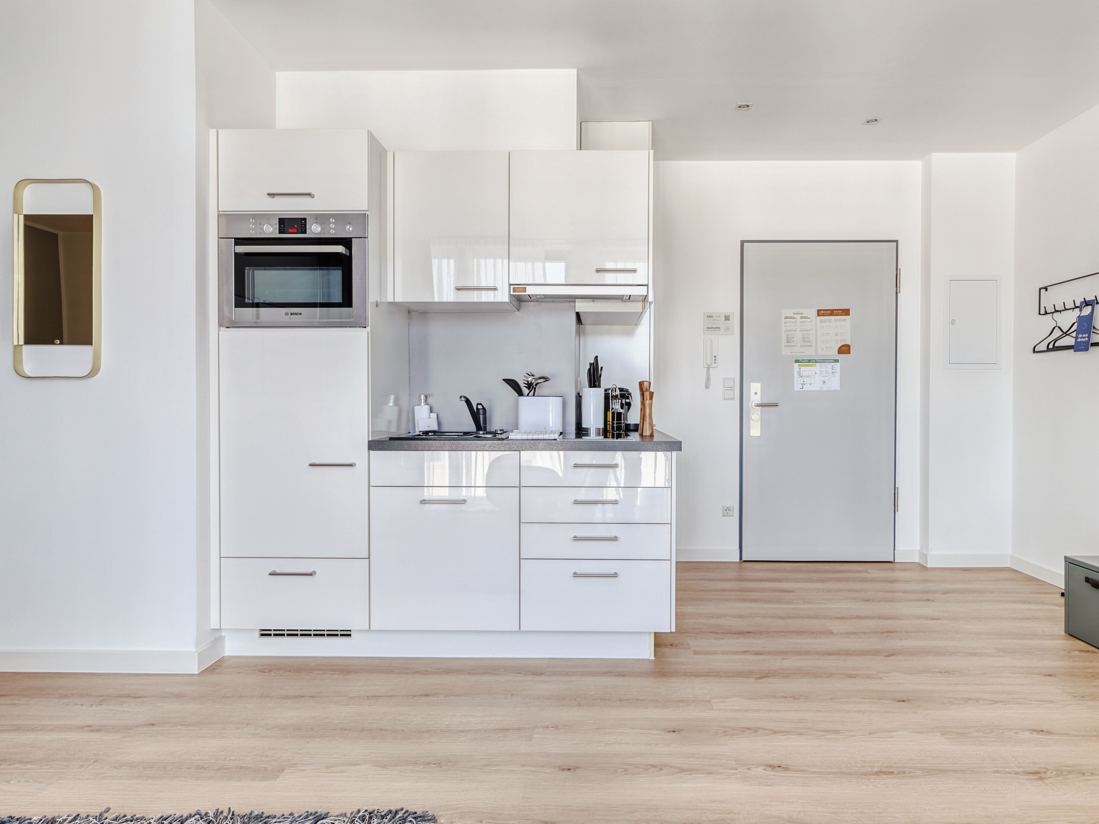 Una cuina moderna amb armaris blancs, un forn Bosch i un frigorífic d'acer inoxidable.