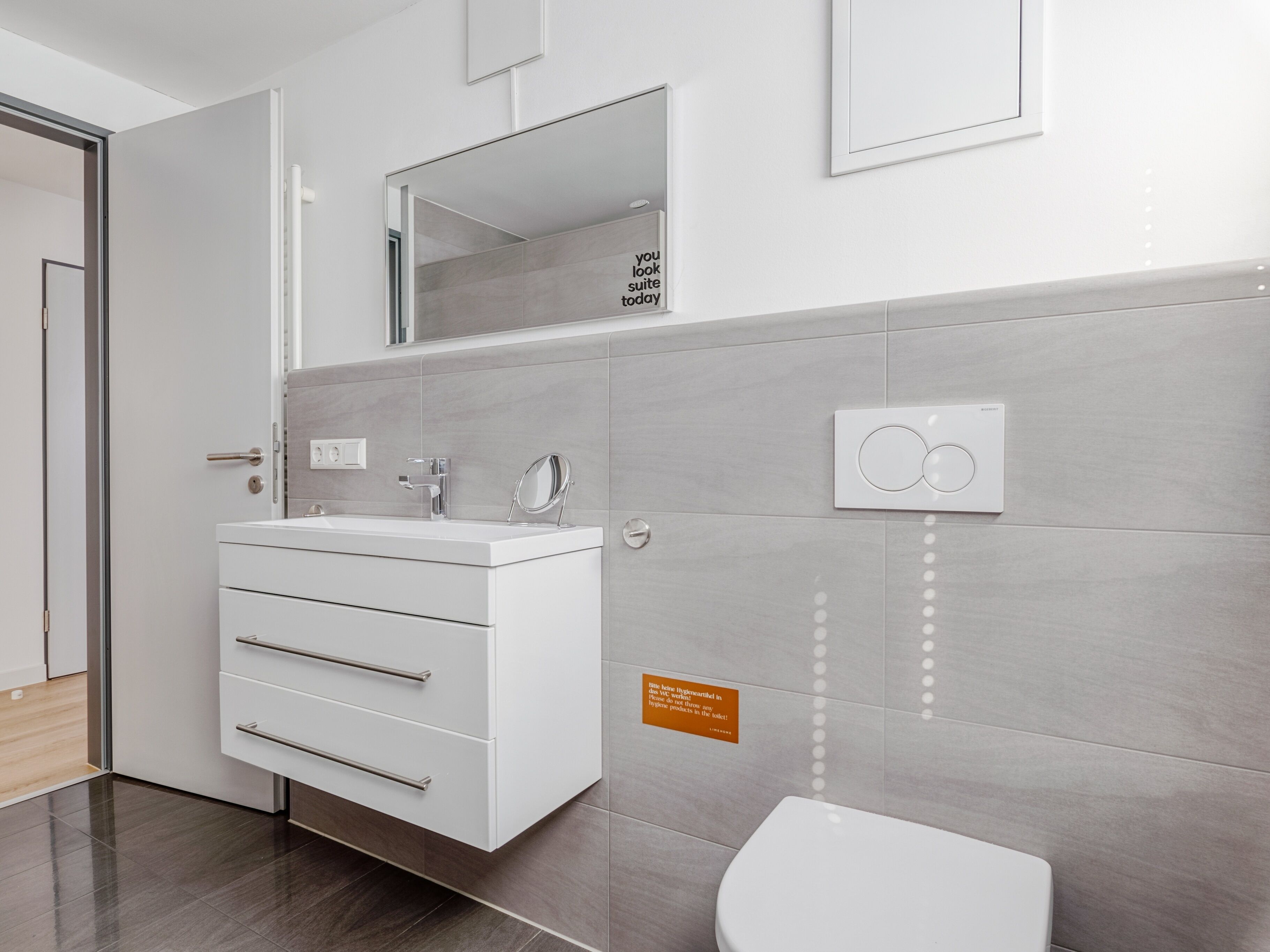 A modern bathroom with a white vanity, a mirror, a toilet, and a wall-mounted light fixture.