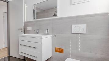 A modern bathroom with a white vanity, a mirror, a toilet, and a wall-mounted light fixture.