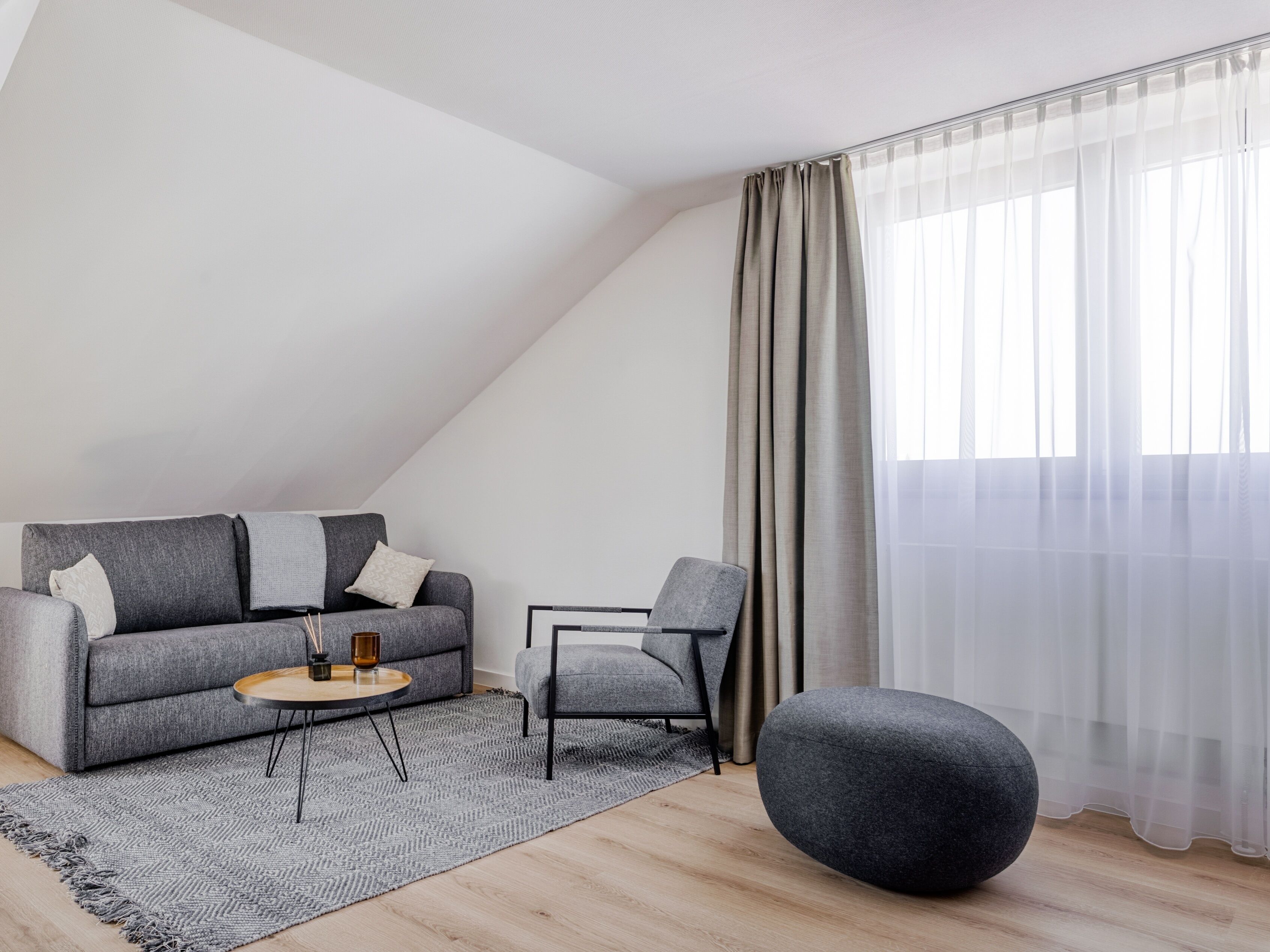 Ein modernes Wohnzimmer mit einem grauen Sofa, einem runden Couchtisch, einem grauen Sessel und einem schwarzen Ottomanen.