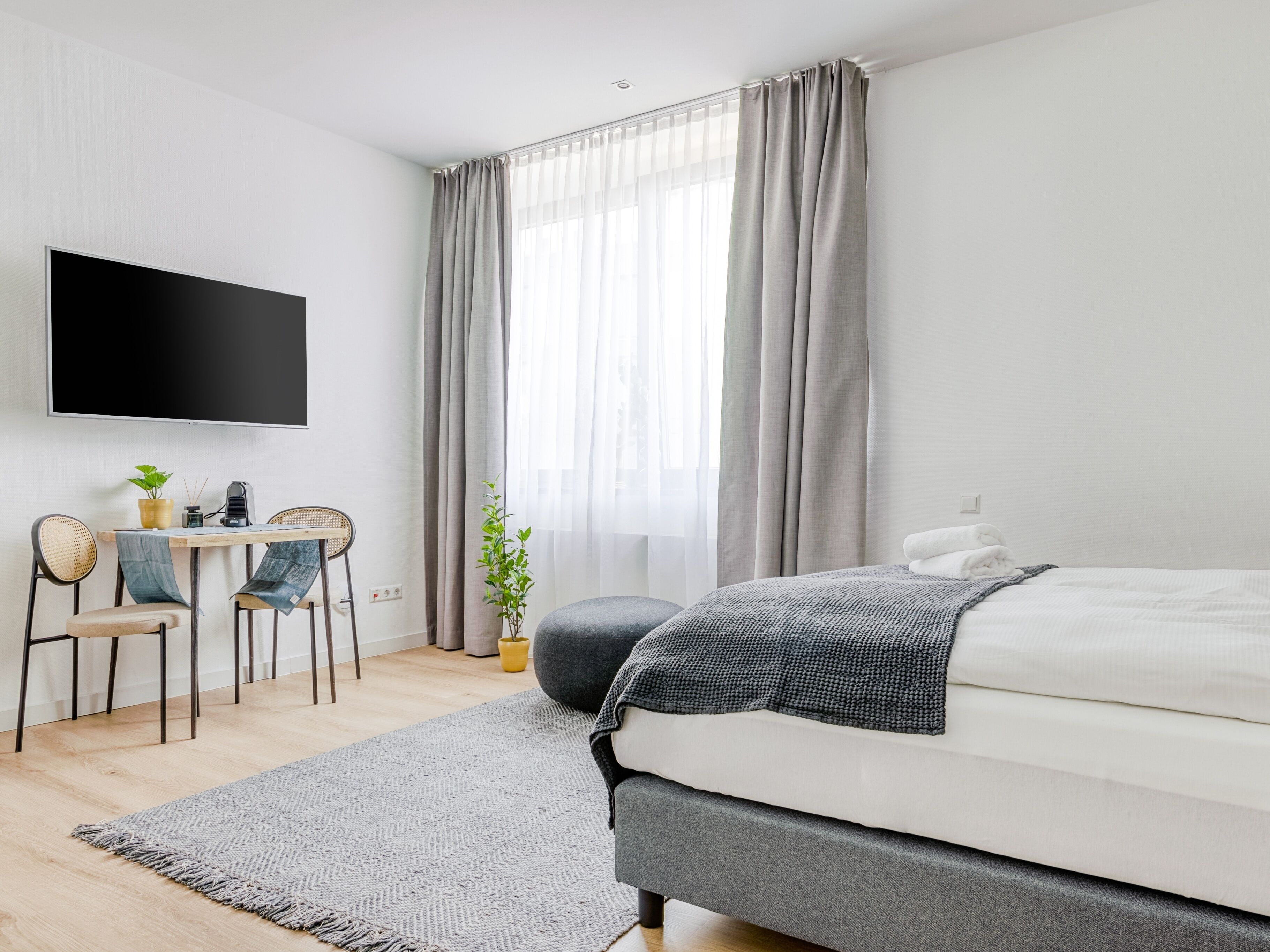 Een moderne slaapkamer met een bed, een bureau met stoel, een televisie en een raam met gordijnen.