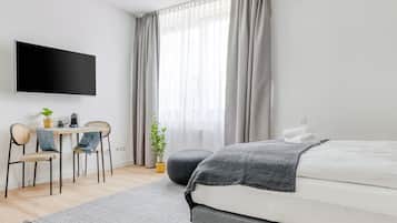 Een moderne slaapkamer met een bed, een bureau met stoel, een televisie en een raam met gordijnen.