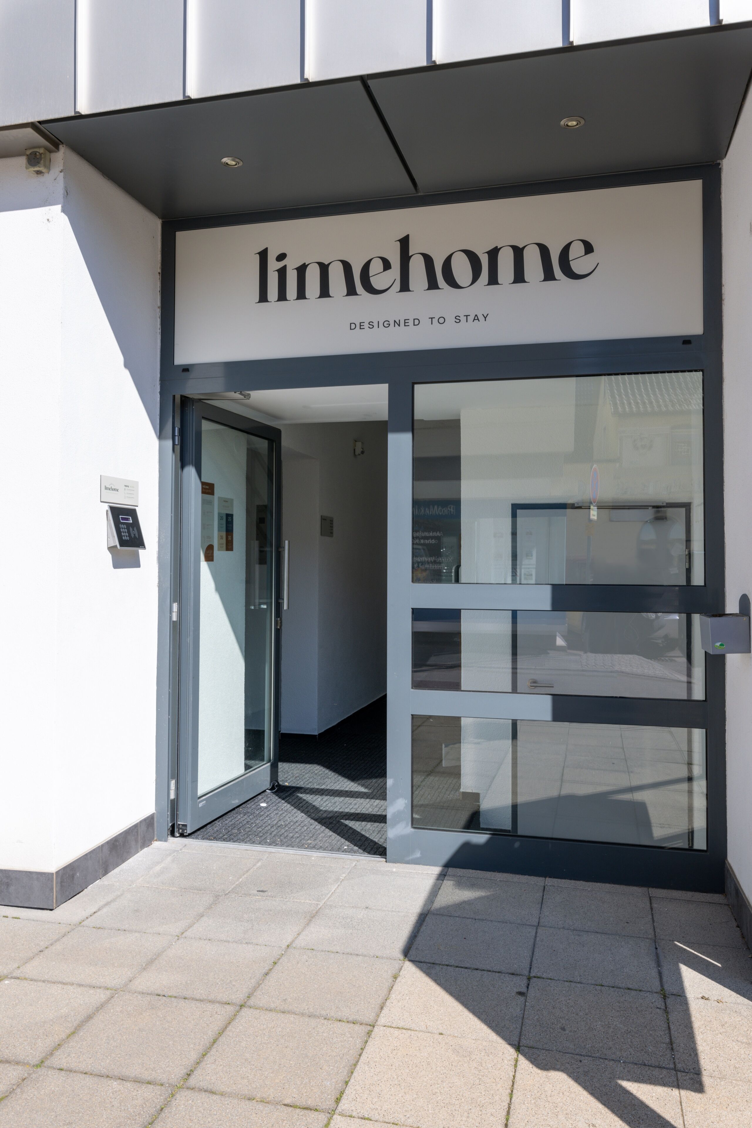 Une entrée moderne avec une porte en verre et une enseigne indiquant : « limehome, conçu pour un séjour prolongé ».